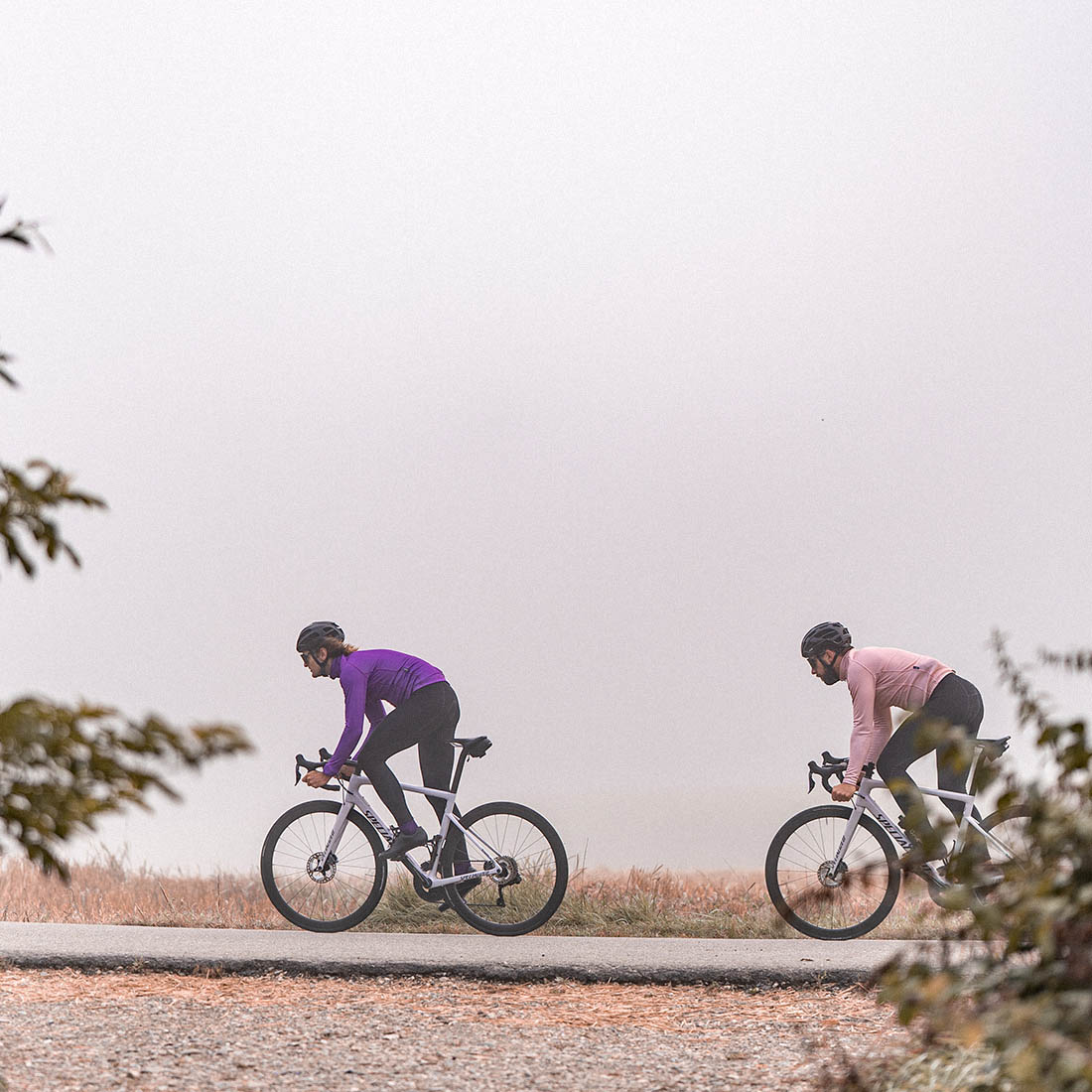 Two cyclists on road bikes ride in cool autumn weather dressed in warm autumn clothing by the Luxa brand